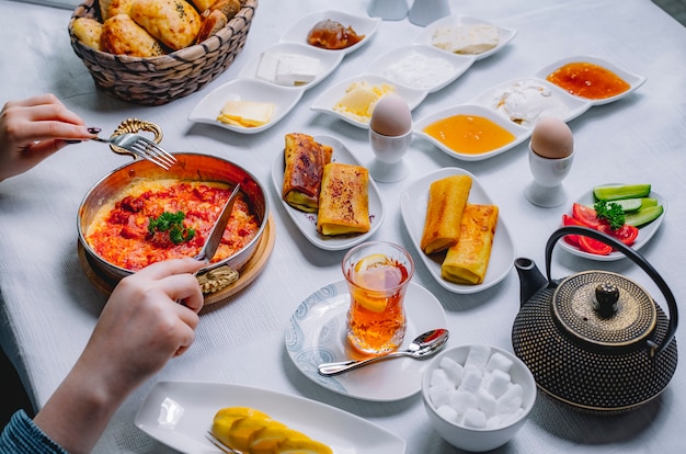 Vue de dessus une femme a des œufs au plat avec des tomates dans une casserole avec des crêpes et un verre de thé