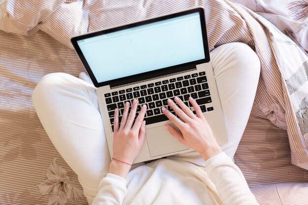 Vue de dessus de la femme avec un ordinateur portable assis sur le lit