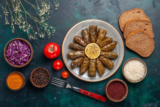 Vue de dessus feuille dolma délicieux repas de viande de l'est roulé à l'intérieur des feuilles vertes avec des tomates et du pain sur le bureau bleu viande nourriture dîner plat santé des légumes