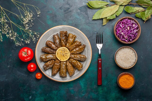 Vue de dessus feuille dolma délicieux repas de viande orientale roulé à l'intérieur de feuilles vertes avec des tomates fraîches sur bleu foncé bureau viande nourriture dîner plat santé végétale