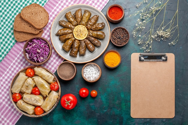 Vue de dessus feuille dolma repas de viande de l'est roulé à l'intérieur de feuilles vertes avec des assaisonnements et du chou dolma sur le plat de dîner de viande de bureau bleu foncé est repas