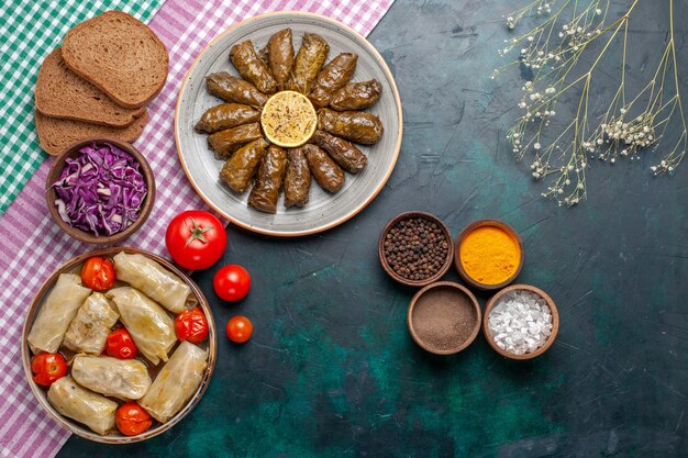 Vue de dessus feuille dolma repas de viande de l'est roulé à l'intérieur de feuilles vertes avec des assaisonnements et du chou dolma sur le plat de dîner de viande de bureau bleu foncé est repas