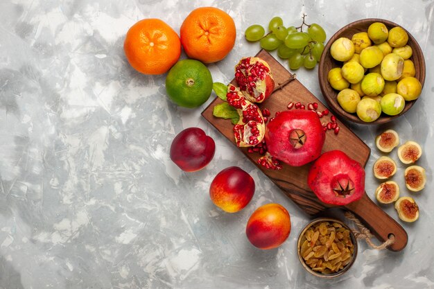 Vue de dessus figues fraîches aux grenades, pêches et raisins sur un bureau blanc