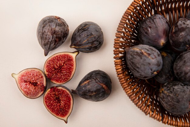 Vue de dessus des figues de mission noires bio sur un seau avec des figues noires isolé sur un mur blanc