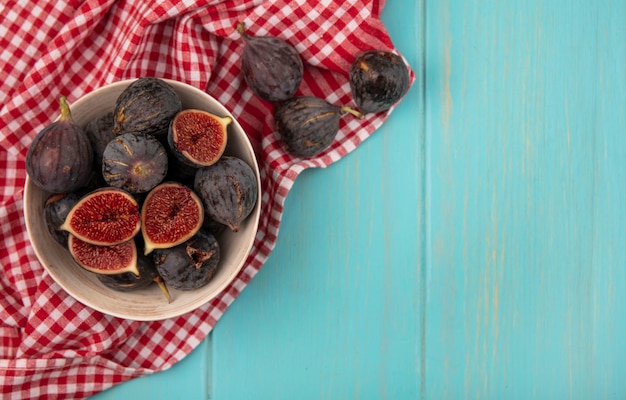 Vue de dessus des figues de mission noires mûres douces sur un bol sur un chiffon vérifié sur un mur en bois bleu avec espace copie