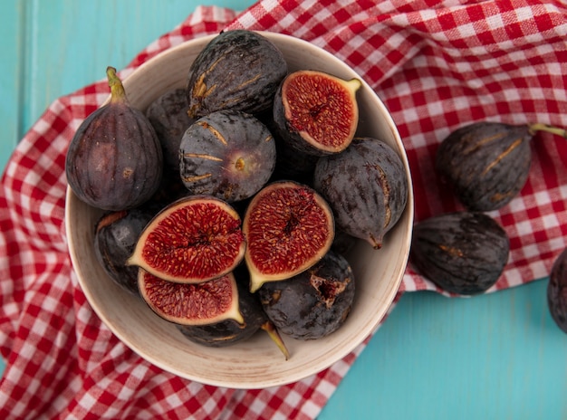 Vue de dessus des figues de mission noires mûres douces sur un bol sur un tissu à carreaux rouge sur un mur en bois bleu