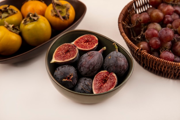 Vue de dessus des figues noires sucrées sur un bol avec des fruits kaki sur un bol sur un mur blanc