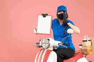 Photo gratuite vue de dessus d'une fille de messagerie émotionnelle portant un masque médical et des gants assis sur un scooter tenant une feuille de papier vide livrant des commandes sur fond de pêche pastel