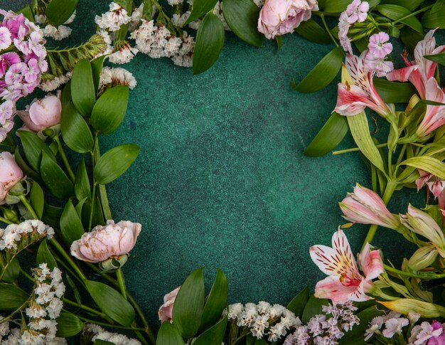 Vue de dessus des fleurs rose clair avec des branches de feuilles sur une surface verte