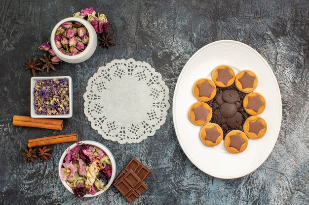 Vue de dessus des fleurs sèches et des biscuits assortis sur plaque blanche et un morceau de dentelle sur fond gris