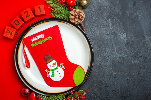 Vue de dessus de fond de nouvel an avec chaussette de Noël sur assiette à dîner accessoires de décoration branches de sapin et numéros sur une serviette rouge sur un tableau noir