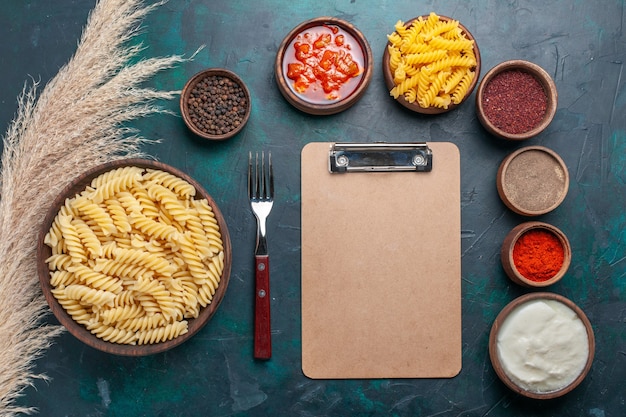 Vue de dessus en forme de pâtes italiennes avec bloc-notes et différents assaisonnements sur le fond bleu foncé