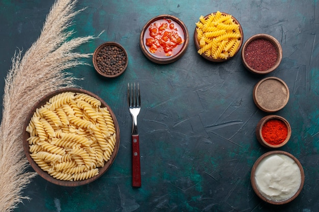 Vue de dessus en forme de pâtes italiennes avec différents assaisonnements sur fond bleu foncé