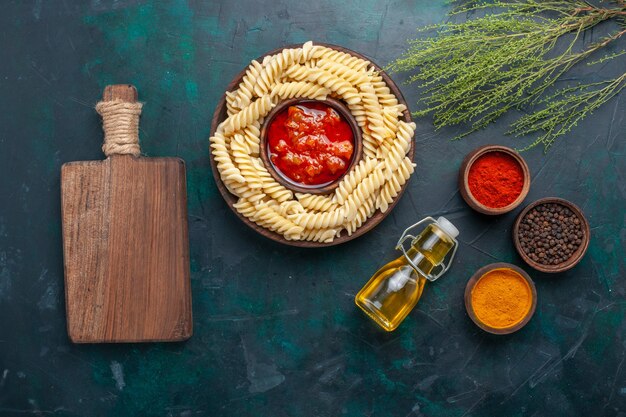 Vue de dessus en forme de pâtes italiennes avec de l'huile et différents assaisonnements sur un bureau bleu foncé