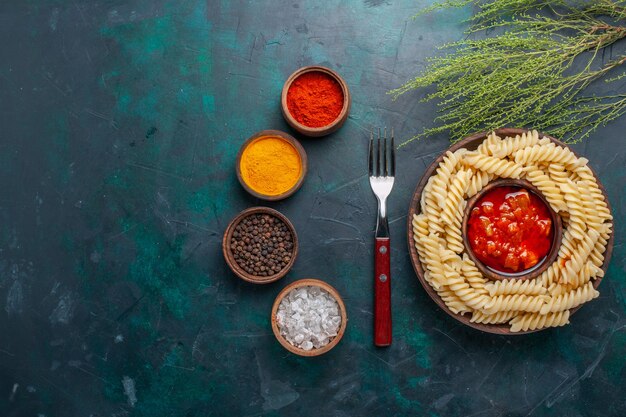 Vue de dessus en forme de pâtes italiennes avec sauce tomate et assaisonnements sur bureau bleu foncé