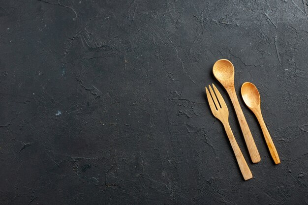 Vue de dessus fourchette et cuillères en bois sur table sombre avec espace libre