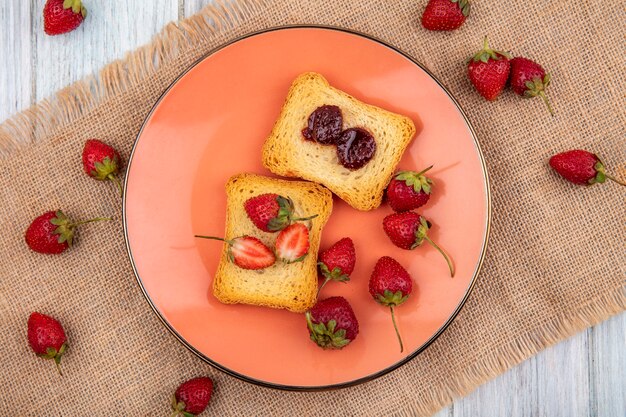 Vue de dessus de la fraise sur une assiette avec des fraises fraîches isolé sur un sac en tissu sur un fond en bois gris