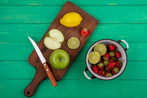 Vue de dessus de la fraise sur une casserole avec de la chaux sur une planche de cuisine en bois sur un fond en bois vert