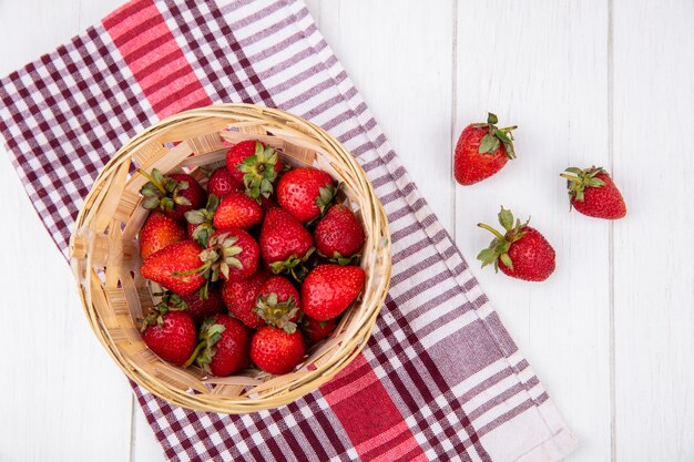 Vue de dessus des fraises dans le panier sur tissu à carreaux et surface en bois