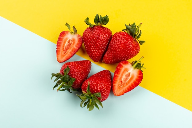 Vue de dessus de fraises entières en tranches moelleux juteux sur le plancher bleu-jaune
