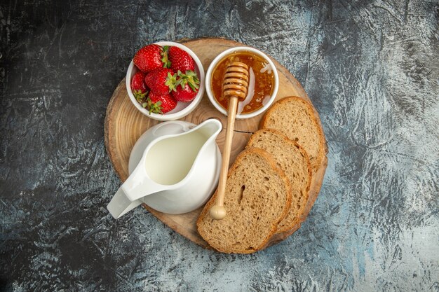 Vue de dessus fraises fraîches avec du miel et du pain sur une surface sombre gelée sucrée de fruits