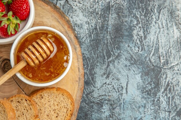 Vue de dessus fraises fraîches avec du pain et du miel sur la gelée sucrée de fruits de surface sombre