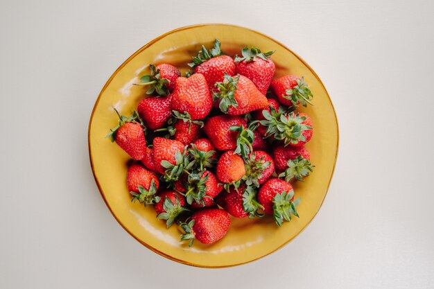 Vue de dessus des fraises mûres fraîches dans une assiette jaune sur blanc