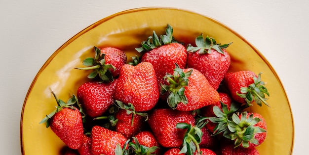 Vue de dessus des fraises mûres fraîches dans une assiette jaune sur blanc