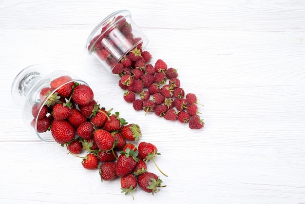 Vue de dessus des fraises rouges fraîches à l'intérieur et à l'extérieur de la plaque sur la lumière blanche, baies de fruits frais moelleux