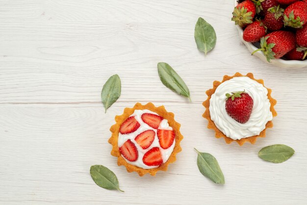 Vue de dessus des fraises rouges fraîches moelleuses et délicieuses baies à l'intérieur de la plaque blanche avec des gâteaux sur la lumière, fruit berry red