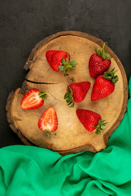 Vue de dessus des fraises rouges tranchées mûres moelleuses sur le bureau en bois marron et sol sombre