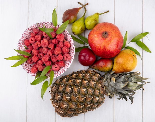 Vue de dessus des framboises dans un bol avec grenade ananas pêche prune sur surface blanche