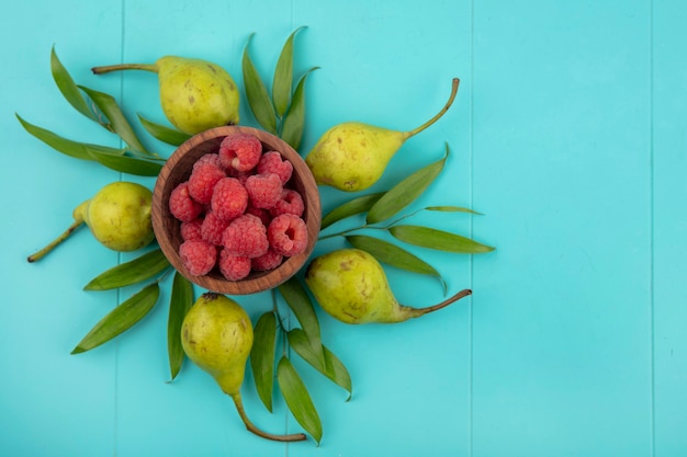 Vue de dessus des framboises dans un bol avec des pêches et des feuilles sur une surface bleue