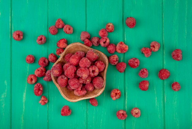 Vue de dessus des framboises dans un bol et sur une surface verte