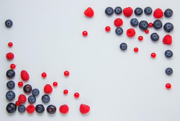 Vue de dessus des framboises dans les coins avec des bleuets, des groseilles sur fond blanc. horizontal