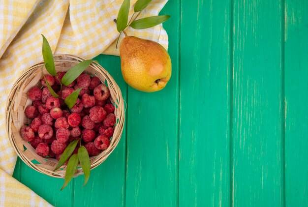 Vue de dessus des framboises dans le panier sur tissu à carreaux avec pêche sur surface verte