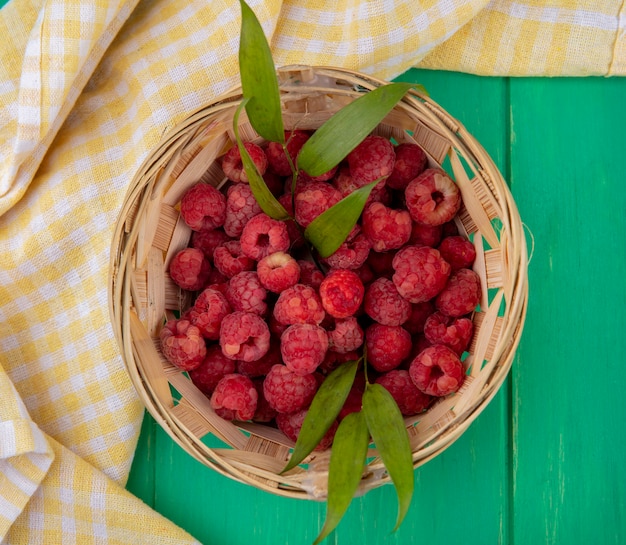 Vue de dessus des framboises dans le panier sur un tissu à carreaux sur une surface verte