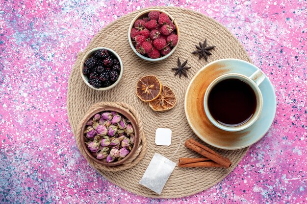 Vue de dessus framboises et mûres baies fraîches avec tasse de thé à la cannelle sur le bureau rose.