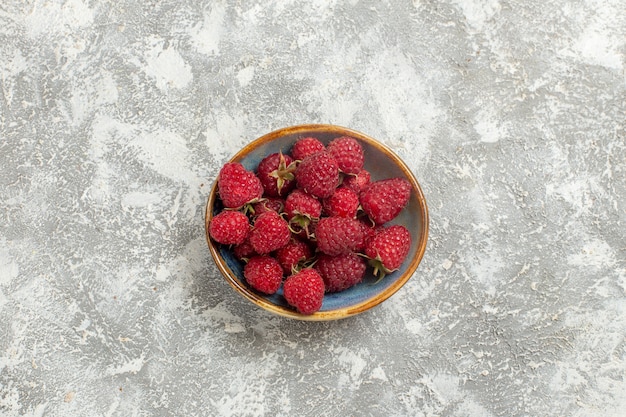 Vue de dessus framboises rouges fraîches à l'intérieur de la plaque sur fond blanc