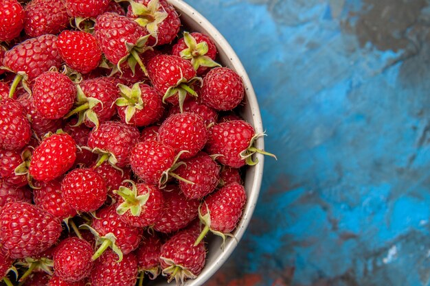 Vue de dessus des framboises rouges à l'intérieur de la plaque sur fond bleu