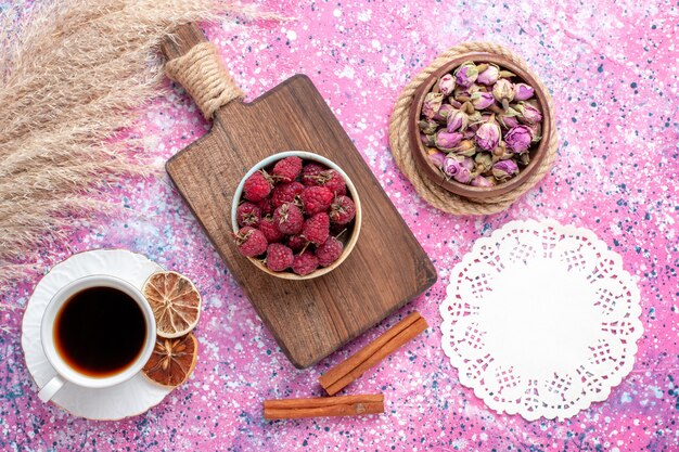 Vue de dessus de framboises savoureuses fraîches à l'intérieur de la plaque blanche avec du thé et de la cannelle sur la surface rose