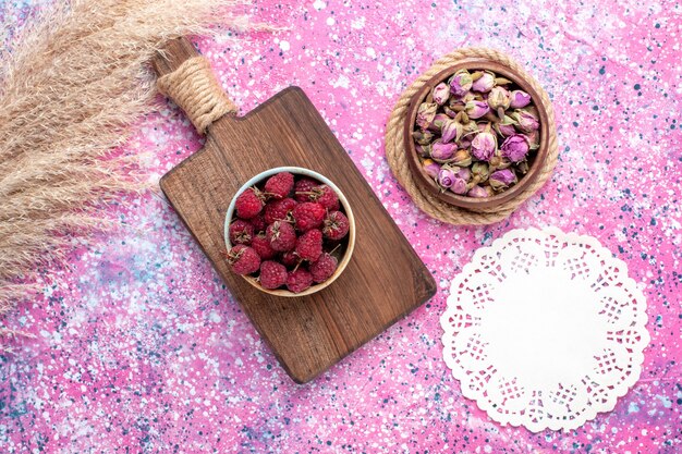 Vue de dessus de framboises savoureuses fraîches à l'intérieur de la plaque blanche sur la surface rose