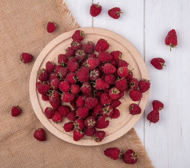 Vue de dessus des framboises sur un support sur une serviette beige sur une surface blanche