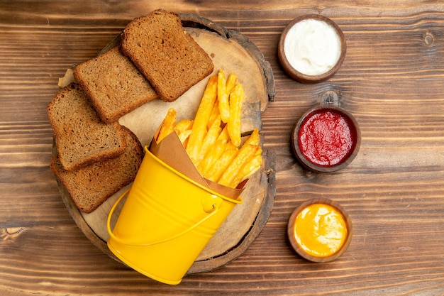 Vue de dessus des frites avec du pain noir et des assaisonnements sur une table marron