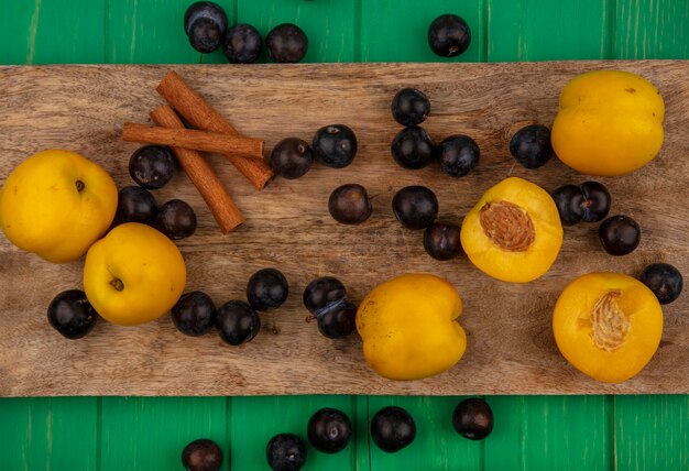 Vue de dessus des fruits comme les abricots et les baies de prunelle à la cannelle sur une planche à découper sur fond vert