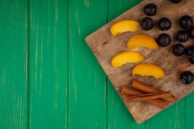 Vue de dessus des fruits comme des abricots en tranches et des baies de prunelle à la cannelle sur une planche à découper sur fond vert avec copie espace