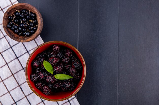 Vue de dessus des fruits comme des bols de prunelle et de mûre sur un tissu à carreaux sur une surface noire