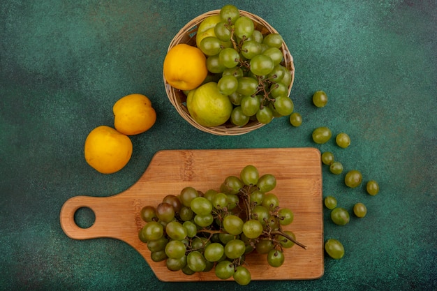 Vue de dessus des fruits comme grappe de raisin sur une planche à découper et nectacot pluot et raisin dans le panier avec des baies de raisin sur fond vert