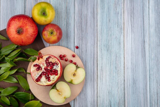 Vue de dessus des fruits comme la moitié de la pomme coupée et la moitié de la grenade sur une planche à découper avec des entiers et des feuilles sur un tissu sur une surface en bois