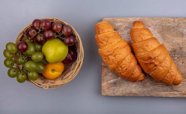 Vue de dessus des fruits comme nectacot de raisin pluot dans le panier et croissants sur une planche à découper sur fond gris